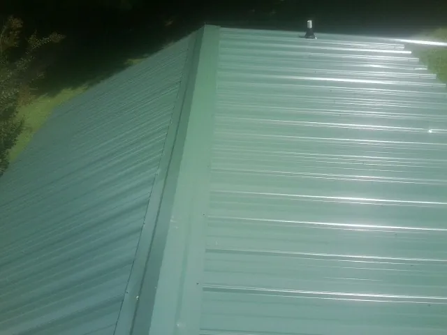 New green metal panels meeting at the ridge of a roof — Flat Roof Repair work by our crew in Middletown
